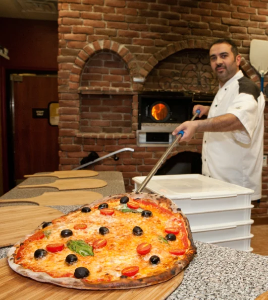 Middle eastern man in Toledo, OH making a wood-fired pizza in his brick oven pizzeria.